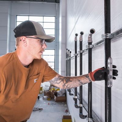 Black Forest Plumbing plumber checking a row of pipe risers strapped to strut channel in a new commercial building